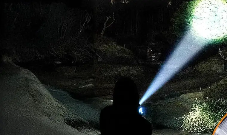 Faisceau serré de la torche éclairant le flanc d'une colline dans la nuit